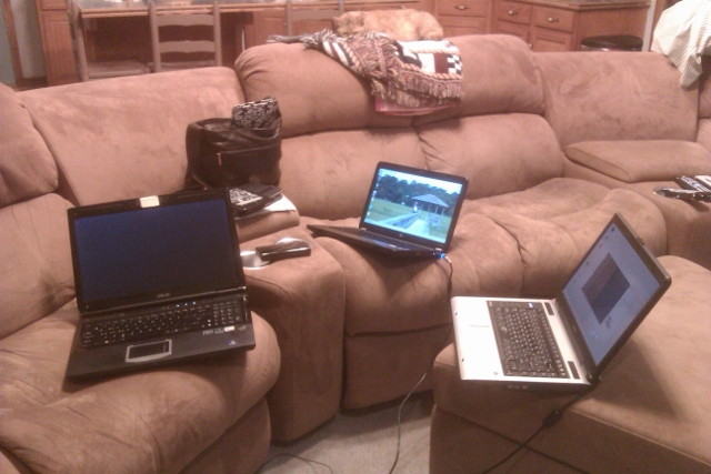3 laptops, a tablet, a Kindle, and a Nintendo DS sitting on a couch.